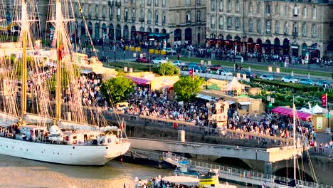 Reunión-De-Personas-En-La-Plaza-Place-De-La-Bourse-Durante-La-Feria-Del-Vino-Con-Un-Velero-Blanco,-Plataforma-Rodante-Aérea-En-Toma