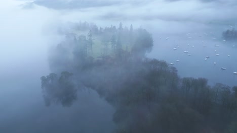 Approaching-drone-shot-of-misty-island-on-Bowness-on-Windermere-Lake,-located-in-Furness-District-in-Cumbria's-Natiional-Park-in-England