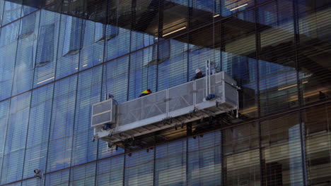 Trabajadores-En-Góndola-Suspendida-Limpiando-Ventanas-De-Vidrio-De-Un-Edificio-Alto