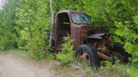 Panning-shot-showing-the-deserted-road-then-an-abandoned-1940s-truck-rusting-away-and-overgrown-with-weeds-and-trees