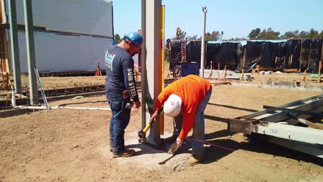 Gimbal-wide-shot-of-construction-workers-using-a-wrench-and-sledgehammer-to-tighten-steel-nuts-and-bolts-at-a-modular-building-site-in-West-Los-Angeles,-California