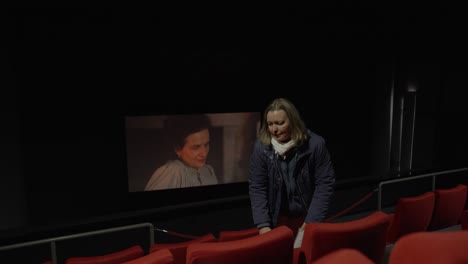 Close-up-shot-of-a-woman-walking-through-a-row-in-the-cinema-with-a-movie-on