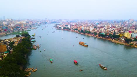 Establishing-aerial-view-Dhaka-cargo-ships-travelling-down-river-passing-colourful-Bangladesh-congested-mega-city