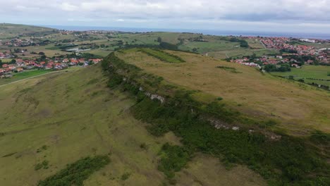 Orbital-drone-flight-over-a-deserted-area-from-the-Iron-Age-in-a-plateau-that-stands-out-from-the-rest-of-the-population-with-urbanizations-between-green-pastures-next-to-the-sea-in-Cantabria-Spain