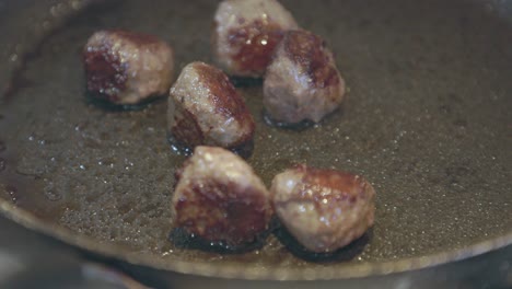 Close-up-shot-of-oil-bubbling-below-meatballs-being-cooked-in-a-frying-pan