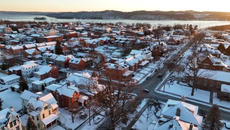 Aerial-view-of-a-snow-dusted-town-at-dusk,-with-a-river-and-hills-in-the-distance