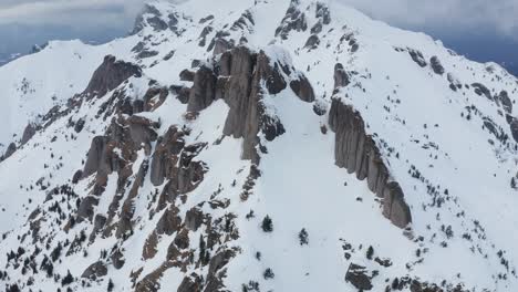 Snow-covered-Ciucas-Mountains-under-cloudy-skies,-aerial-view