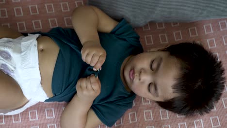 Toddler-getting-nappy-change-on-a-checkered-mat,-playing-with-shirt-button,-overhead-shot