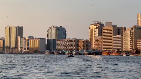 Paseos-En-Bote-En-El-Agua-Del-Canal-Bur-Dubai-Dubai-Creek-En-El-Viejo-Dubai-Con-Vista-Al-Edificio-Antiguo-Con-Gaviotas-Volando