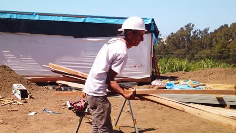 Toma-De-Cardán-De-Un-Trabajador-De-La-Construcción-Que-Lleva-Una-Pila-De-Madera-Y-La-Coloca-En-Una-Rejilla-De-Corte-En-Un-Sitio-De-Construcción-Modular-En-El-Oeste-De-Los-Ángeles,-California.