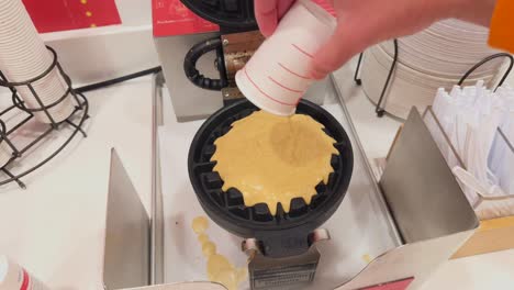 Pouring-batter-from-paper-cup-into-Belgian-waffle-maker-at-an-American-hotel