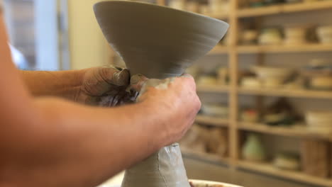 Potter-gently-lifting-handmade-clay-bowl-from-excess-material-on-pottery-wheel-turntable