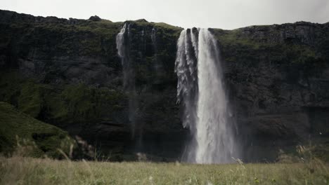 Weite-Dolly-Aufnahme-Einer-Absolut-Atemberaubenden-Szene-Mit-Einem-Wasserfall,-Klippen-Und-Einem-Grünen-Feld