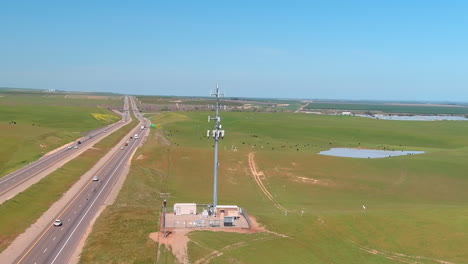 Una-Carretera-Junto-A-Una-Instalación-Industrial-Con-Una-Torre-De-Comunicación-En-Un-Día-Soleado,-Ganado-Pastando-Cerca,-Vista-Aérea