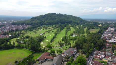 Aerial-view-of-a-green-golf-course-on-a-sunny-day-with-a-small-pond-in-the-middle-of-city