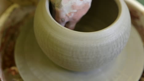 Potter-hands-applying-finishing-touch-to-completed-handmade-flowerpot-on-workshop-pottery-wheel