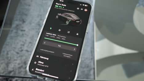 Smartphone-Auf-Glastisch-Mit-Tesla-App-Beim-Ladevorgang