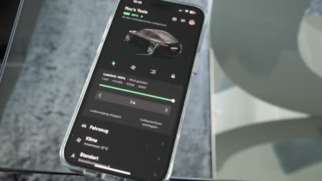 Smartphone-Sobre-Una-Mesa-De-Cristal-Con-La-Aplicación-Tesla-En-El-Proceso-De-Carga.