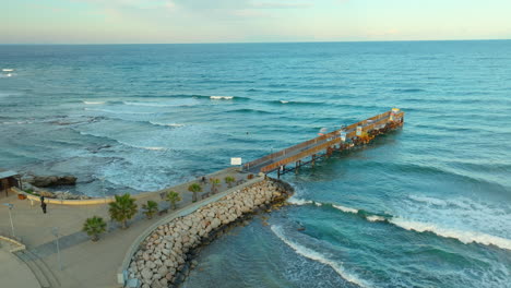 Aerial-view-of-a-wooden-pier-in-Protaras,-Cyprus,-with-wavy-sea