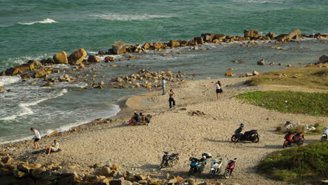 Pueblo-Vietnamita-Relajándose-Junto-Al-Mar-En-Una-Playa-De-Arena-Con-Sus-Scooters-Estacionados-Cerca-En-Nha-Trang-Vietnam