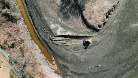 Aerial-bird's-eye-view-static-top-down-shot-of-a-yellow-bulldozer-operating-on-sediment-deposits