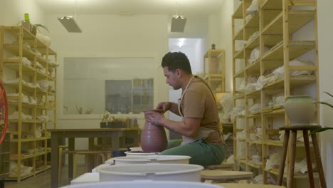 Joven-Artesano-Artesano-Dando-Forma-A-Una-Escultura-De-Jarrón-Hecha-A-Mano-En-Un-Torno-De-Alfarería-De-Taller