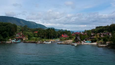 Aerial-drone-of-Lake-Toba-with-village,-mountains,-and-blue-water-in-Sumatra,-Indonesia