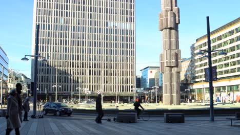 La-Gente-Y-Los-Coches-Pasan-Por-El-Obelisco-En-La-Plaza-De-La-Ciudad-Sergels-Torg,-Estocolmo