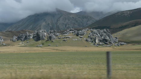 Slow-motion-driving-by-large-boulders-in-a-field-with-mountains-in-the-background---Castle-Hill,-New-Zealand