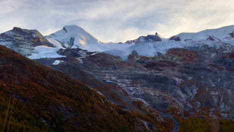 Sunset-golden-hour-Swiss-Alps-Saas-Fee-Saastal-Plattjen-Zermatt-glacier-Switzerland-summer-fall-autumn-light-on-mountain-peaks-yellow-lark-trees-cloudy-stunning-cinematic-slow-pan-to-the-left