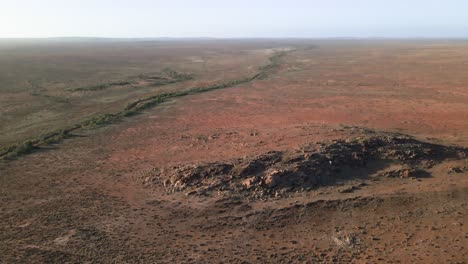 Luftaufnahme-Des-Australischen-Outbacks-Mit-Roten-Felsen-Und-Einem-Von-Bäumen-Gesäumten-Flussbett