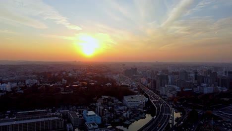 Sunrise-over-city-skyline-with-rays-peeping-above-buildings,-early-morning,-aerial-view