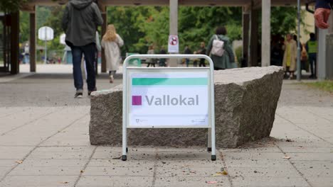 People-move-by-polling-station-sign-on-election-day-in-Sweden,-closeup