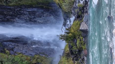 Ein-Vertikaler-Blick-Auf-Den-Mächtigen-Wasserfall-Thunder-Creek-Falls,-Der-In-Einen-Von-Gletschern-Gespeisten-Fluss-Fließt,-Der-Von-üppigem-Regenwald-Umgeben-Ist