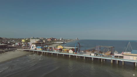 An-aerial-establishing-shot-captures-the-atmosphere-of-The-Pleasure-Pier-as-the-late-afternoon-sun-casts-a-warm-glow-over-Seawall-Blvd-in-Galveston,-Texas
