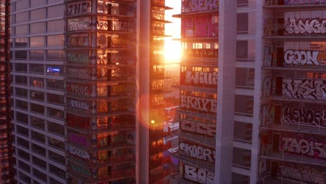 Toma-Aérea-De-Primer-Plano-Ascendente-Con-Destellos-De-Lente-De-Los-Coloridos-Murales-De-Graffiti-En-Las-Torres-Inacabadas-De-La-Plaza-Oceánica-Al-Atardecer-En-El-Centro-De-Los-Ángeles,-California