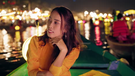 Mujer-Vestida-De-Amarillo-Ao-Dai-En-Un-Barco-En-El-Río-Hoi-An-Por-La-Noche,-Luces-Reflejadas-En-El-Agua,-Humor-Contemplativo,-Primer-Plano