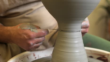 Potter-carefully-removing-completed-bowl-with-tread-on-workshop-pottery-wheel