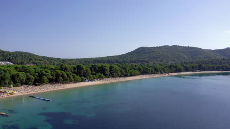 Aerial:-Orbit-shot-of-Koukounaries-beach-in-Skiathos,-Greece-with-lush-pine-tree-forest-and-turquoise-water