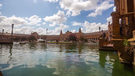 Boats-sailing-time-lapse-tourists-along-Spanish-travel-landmark-Plaza-de-España-traditional-gondolas,-close-up-water-shot-reflected-colonial-architecture,-Spain-summer