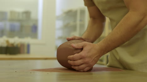 Potter-shaping-and-rolling-raw-clay-preparing-to-create-handmade-vase-in-workshop