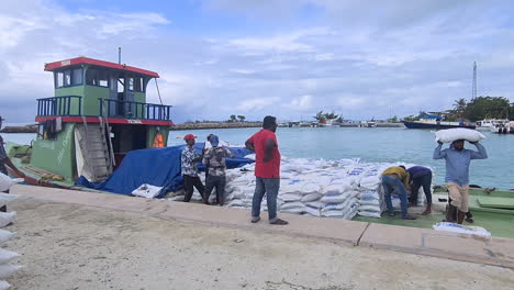 Isla-Maldivas,-Trabajadores-Descargando-Envíos-Desde-Un-Pequeño-Buque-De-Carga,-Sacos-Para-El-Sitio-De-Construcción