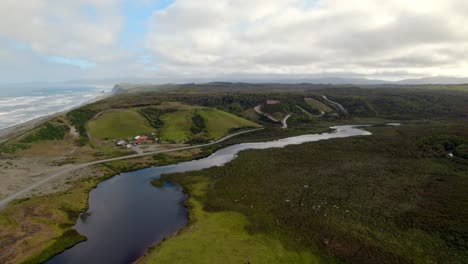 Aerial-viewt-of-Small-houses-at-river-shore-by-the-Pacific-Ocean,-Scenic-landscape,-Cucao