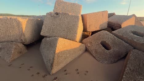Concrete-blocks-and-cubes-along-the-beach,-where-coastal-defense-structures-are-partially-submerged-in-sand