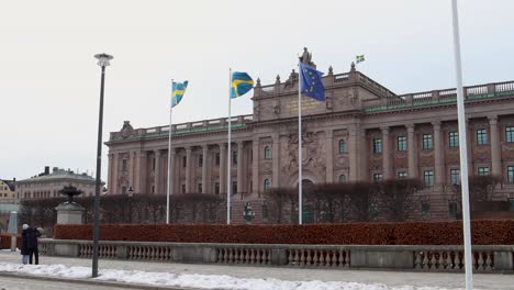 Swedish-Parliament-with-flags-of-Sweden-and-EU-in-foreground,-winter