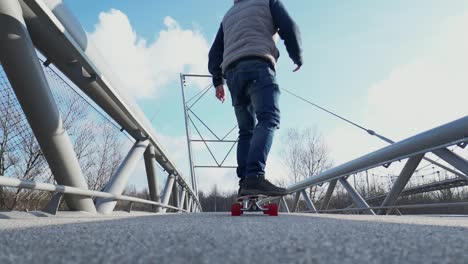 Un-Hombre-En-Un-Longboard-Pasa-Junto-A-La-Cámara-Y-Llega-A-Un-Puente-Peatonal