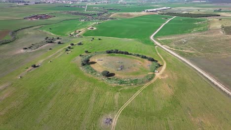 Vuelo-Orbital-Con-Drone-Viendo-Los-Restos-De-Un-Gran-Dolmen-Donde-Hoy-Se-Utiliza-Para-La-Agricultura-Con-Varios-Caminos-En-Un-Entorno-De-Verdes-Campos-De-Cultivo-En-Una-Mañana-De-Invierno-En-Toledo,-España