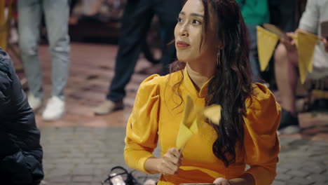 Attractive-Vietnamese-woman-in-yellow-traditional-outfit-playing-game-with-yellow-flag-on-Hoi-An-street