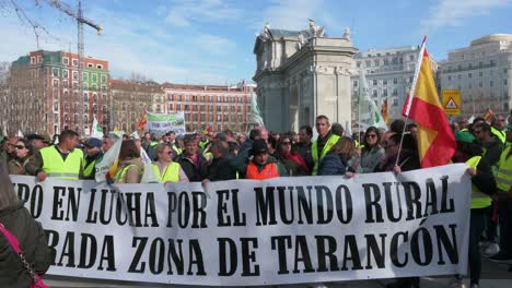 Spanish-farmers-and-agricultural-union-protesters-hold-a-banner-as-they-gather-at-Puerta-de-Alcalá,-in-Madrid-to-protest-against-unfair-competition-and-agricultural-policies