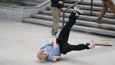 A-Young-Man-in-Blue-Shirt-Wipes-Out-Crashes-in-front-of-a-crowd-of-teenagers-onlookers-after-riding-his-skateboard-down-a-concrete-rail-at-a-skate-park